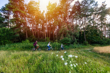 Happy family riding bikes on week-end in countryside at sunset