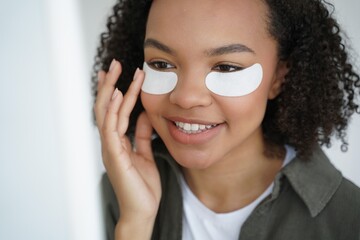 Young biracial girl applying under eye patches for healthy fresh face skin. Skincare, beauty routine