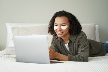 Biracial girl with under eye patches on face work at laptop. Morning facial skincare routine, beauty