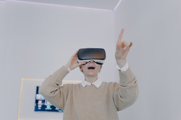Young white woman in VR glasses in futuristic office. Girl in VR goggles is pointing with finger.