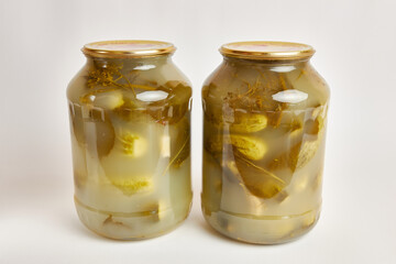 Glass jars with canned cucumbers on a white background.