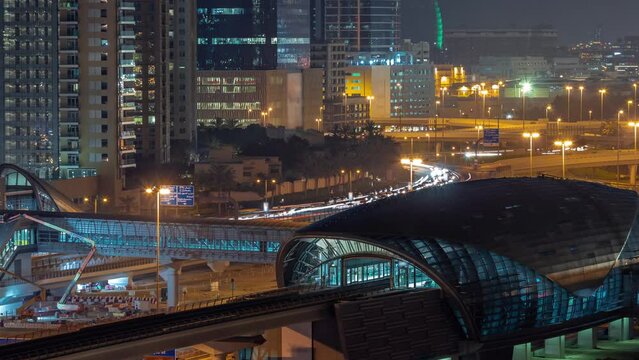 Futuristic building of Dubai metro station and luxury skyscrapers behind in Dubai Marina aerial night timelapse. Traffic on Sheikh Zayed road highway near media city, United Arab Emirates