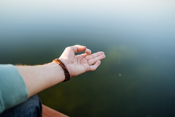 The hand shows the element of yoga, the practice of meditation in silence, the fingers of the hand against the background of the water, yoga on the sea in the summer, put the symbol on the hand