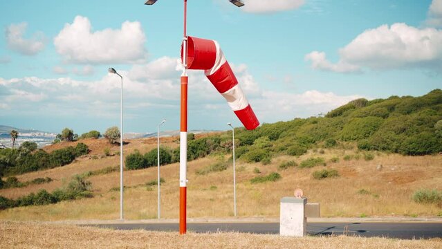 Wind sock fly. Summer hot day on private sporty airport with abandoned windsock, wind is blowing and windsock is lazy moving. Windsock with cloud sky mountain and road with cars on background 