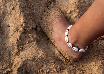 Woman with a conch shell foot bracelet pinching the sand