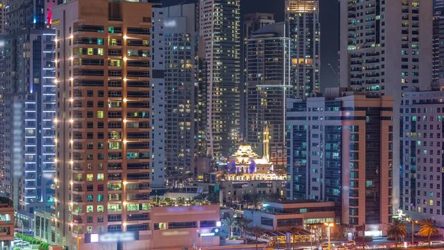 Dubai Marina skyline with Mohammad Bin Ahmed Al Mulla mosque aerial timelapse at night. Skyscrapers with glowing windows on a background with traffic on the road