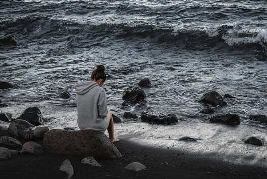 Girl sitting on a rock on a beach of sand and stones