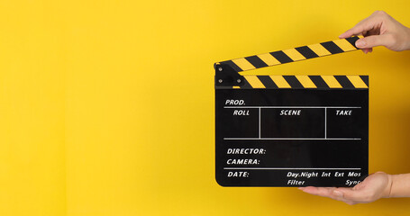 The man's hands are holding black with yellow clapper board or movie slate on yellow background..