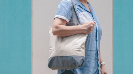 Midsection of plus size woman carrying reusable canvas eco friendly tote bag on pastel blue and...