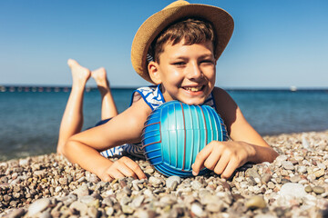 Happy boy has water polo ball on the beach. Looking at camera. Concept of travel, tourism, family.