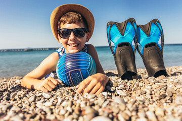 Happy boy has water polo ball and scuba gear on the beach. Looking at camera. Concept of travel,...