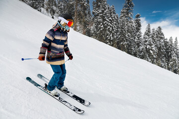 A skier in a striped jacket goes down the slope of the ski resort. Active winter recreation, skiing on a sunny day. woman skier