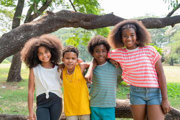 Portrait of happy African American children standing and embracing together in the park.