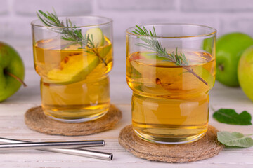 Juice from green apples in glasses with a sprig of rosemary.
