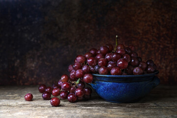 Fresh red grape in a blue bowl on wooden board table and background - dark and moody