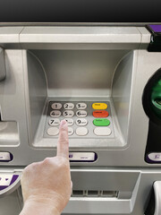 A man's hand is about to enter a code on an ATM's numeric keypad
