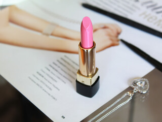 Female cosmetic like a pink  lipstick on the pastel background with silver jewerly on the table