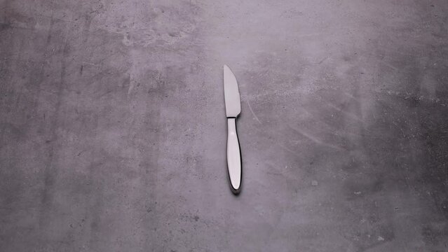 A glossy knife is spinning on the table, a video of cutlery on a gray background.