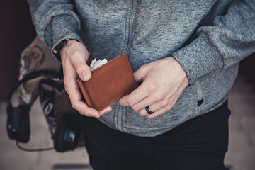 A man in a gray hoodie is holding a brown leather wallet. Lifestyle. Horizontal orientation, no face, copy space