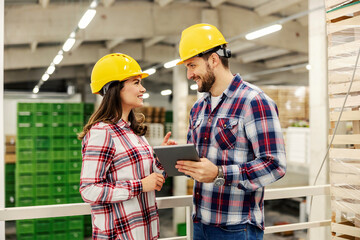 Two warehouse supervisors in facility making a checklist on tablet while looking at each other.