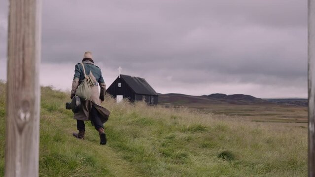 Man with a Sack Bag and Banjo Case Walks Along the Path Through Green Meadow