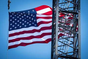 A construction site crane flying a United States Flag in the background with a clear blue sky on a...