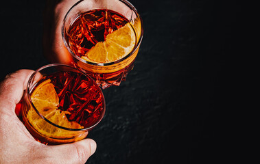 Close up of mens and women's hands clinking the glasses with Negroni cocktails on a black...