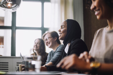 Smiling businesswoman wearing headscarf sitting with colleagues in creative office