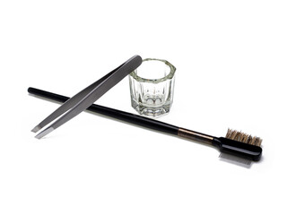 Eyebrow tool, glass container for thinning paint, tweezers and a double brush on a white background