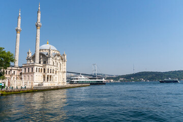 Fototapeta na wymiar Ortakoy Mosque, with the Bosphorus to the side, and the bridge that crosses it in the background of the image, with the afternoon sun on a sunny day.