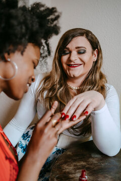 Young woman applying nail polish to non-binary friend at home