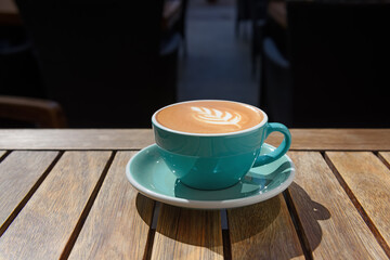 Cup of aromatic hot coffee on wooden table in outdoor cafe