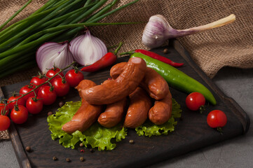 smoked sausages on a wooden board, decorated with fresh vegetables