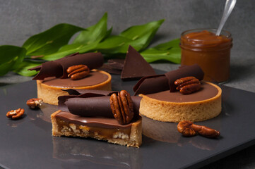 Crispy shortbread tartlet stuffed with fried pecans and creamy caramel, decorated with ganache on...