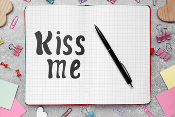 Phrase Kiss me written in notebook and stationery on light grey stone table, flat lay
