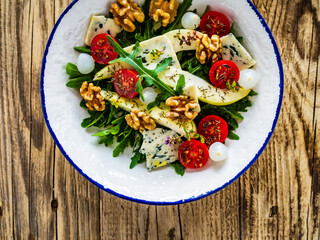 Fresh salad - blue cheese, cherry tomatoes, pear,  leafy vegetables and walnuts on wooden background
