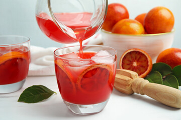 Pouring tasty sicilian orange juice into glass on white table