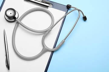 Clipboard with stethoscope and pen on light blue background, top view. Space for text
