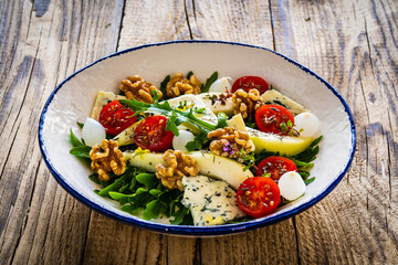 Fresh salad - blue cheese, cherry tomatoes, pear,  leafy vegetables and walnuts on wooden background
