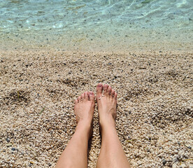 Tanned legs of a girl on the beach near the water