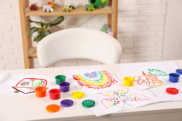 Cute children's drawings and set of paints on white table in room