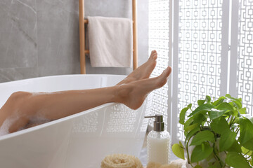 Woman taking bath and shower gel indoors, closeup