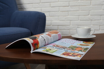 Open magazine and cup of coffee on wooden table in room