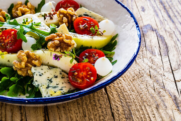 Fresh salad - blue cheese, cherry tomatoes, pear,  leafy vegetables and walnuts on wooden background
