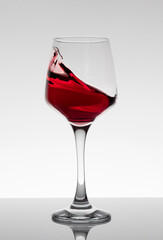 A glass of red wine in movement on a white background.