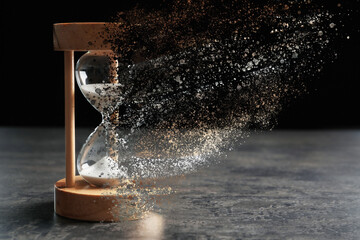 Time is running out. Hourglass vanishing on grey table against black background