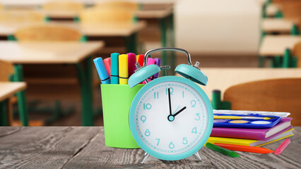 Turquoise alarm clock and different stationery on wooden table in classroom