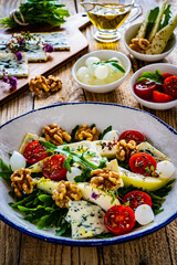 Fresh salad - blue cheese, cherry tomatoes, pear,  leafy vegetables and walnuts on wooden background
