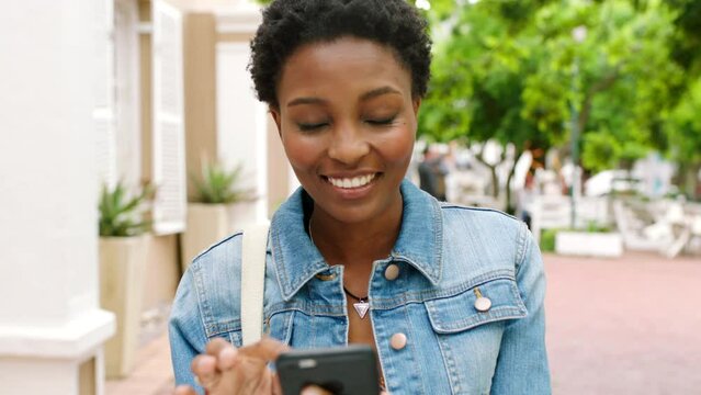 Young woman using a phone outside in the city. Stylish african woman browsing online and checking social media on a mobile device. Single female swiping on a dating app looking for a partner or date