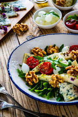 Fresh salad - blue cheese, cherry tomatoes, pear,  leafy vegetables and walnuts on wooden background

